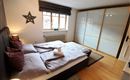 Ein gemütliches Schlafzimmer mit einem Doppelbett und zwei Kissen. Der Raum hat große Fenster und moderne Möbel, die eine helle und einladende Atmosphäre schaffen.