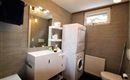 Ein modernes Badezimmer mit einer Waschmaschine, einem Spiegel und einem schlichten Waschbecken. Die Wände sind in neutralen Tönen gehalten, was einen eleganten Look erzeugt.