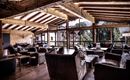 Ein gemütliches Lounge-Ambiente mit Holzdecke und großen Fenstern. Die Einrichtung besteht aus bequemen Sesseln und einem einladenden Tisch.