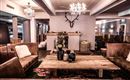 Eine stilvolle Lounge mit gemütlichen Sofas und einem Holztisch. An der Wand hängt ein Geweih, und mehrere Kronleuchter sorgen für eine angenehme Beleuchtung.
