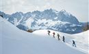 Eine Gruppe von Menschen beim Skifahren in schneebedeckten Bergen. Im Hintergrund sind beeindruckende Felsformationen sichtbar.