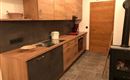 Eine moderne Küche aus Holz mit grauen Schränken und einem hellen Boden. Die Ausstattung umfasst eine Spüle, einen Herd und einen Holzofen.