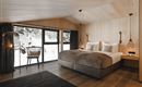 Ein modernes Schlafzimmer mit Holzverkleidung und großen Fenstern. Der Blick zeigt verschneite Landschaften und eine gemütliche Einrichtung.