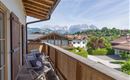 Ein schöner Balkon mit Holzmöbeln und Blick auf die Berge. Im Hintergrund sind grüne Wiesen und Häuser zu sehen.