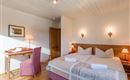 Ein gemütliches Schlafzimmer mit zwei Betten und einem Schreibtisch. Warmes Licht und Holzdetails schaffen eine einladende Atmosphäre.