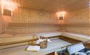 Eine gemütliche Sauna mit Holzwänden und Bänken. In der Ecke stehen ein Eimer und ein Handtuch.