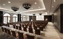 An elegant conference room with rows of chairs and a large screen. Large windows provide plenty of natural light.