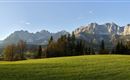 Eine malerische Landschaft mit grünen Wiesen und beeindruckenden Bergen im Hintergrund. Der Himmel ist klar und vermittelt eine friedliche Atmosphäre.
