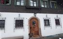 Ein traditionelles Haus mit einem Holztür und großen Fenstern. Es liegt in einer verschneiten Umgebung.