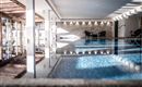 Ein eleganter Innenpool mit Glaswänden und stilvollen Holzdetails. Zwei Stühle stehen am Beckenrand in einer ruhigen Atmosphäre.