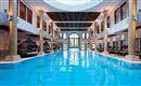 An elegant indoor pool with clear, blue water and stylish columns. The large window front lets in plenty of daylight and creates a relaxing atmosphere.
