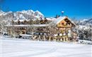 Ein schönes Berghotel im Schnee, umgeben von beeindruckenden Bergen. Der klare blaue Himmel und die schneebedeckte Landschaft sorgen für eine idyllische Winteratmosphäre.