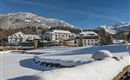 Eine Winterlandschaft mit schneebedeckten Bergen und einem Hotel. Der Himmel ist klar und blau, was einen schönen Kontrast zur weißen Schneedecke bildet.