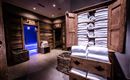 Ein stilvolles Spa mit einem Holzschrank voller gefalteter Handtücher. Im Hintergrund sind zwei Türen sichtbar, die zu einem Wellnessbereich führen.