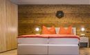Ein modernes Schlafzimmer mit einem großen Bett und leuchtend orangefarbenen Kissen. Die Wände sind aus Holz, und es gibt eine stilvolle Nachtkommode.