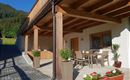 Eine moderne Terrasse mit einem Tisch und Stühlen, umgeben von Pflanzen. Im Hintergrund sind Berge und ein klarer Himmel zu sehen.