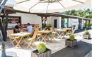 Eine einladende Terrasse mit Holzmöbeln und Sonnenschirmen. Zwei Gäste genießen ihre Zeit in einem gemütlichen Außenbereich.