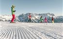 Eine Gruppe von Skifahrern auf einer schneebedeckten Piste. Im Hintergrund sind beeindruckende Berge sichtbar.
