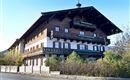 Ein traditionelles alpenländisches Holzhaus mit großen Balkonen. Das Gebäude ist von Bäumen und Sträuchern umgeben.