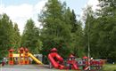 Ein bunt gestalteter Spielplatz mit Rutschen und Spielgerüsten. Umgeben von Bäumen und einer entspannten Landschaft.