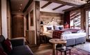 Ein gemütliches Schlafzimmer mit Holzverkleidung und einem großen Bett. Helle Fenster bieten einen Blick nach draußen und der Raum ist stilvoll mit modernen und rustikalen Elementen eingerichtet.