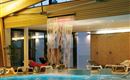 Ein entspannendes Hallenbad mit einem Wasserfall und Liegen zum Relaxen. Das Licht sorgt für eine angenehme Atmosphäre.