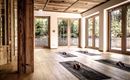 Ein heller Yogaraum mit Holzfußboden und großen Fenstern. Auf dem Boden liegen Yogamatten und Blöcke, um eine entspannte Atmosphäre zu schaffen.