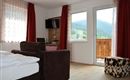 Ein gemütliches Zimmer mit einem Sofa und einem Bett. Große Fenster bieten einen Blick auf die grüne Landschaft.