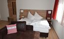 Ein gemütliches Schlafzimmer mit einem Doppelbett und rustikalem Holzdesign. Neben dem Bett steht ein dunkles Sofa mit einem dekorativen Kissen.